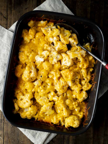 Low-carb keto cauliflower mac and cheese bake with a bubbly, golden cheese crust served in a dark ceramic pan.