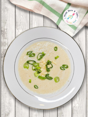 The easiest homemade corn soup recipe served in a white ceramic bowl with green onion garnish on a light wooden table.