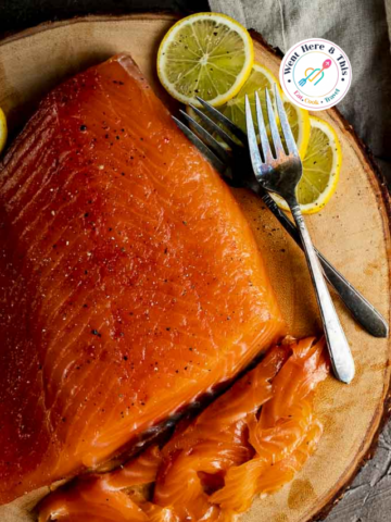 Top-down view of vibrant orange cured gravlax salmon, thinly sliced on a rustic wood board with lemon wedges and black pepper. A high-quality homemade seafood appetizer tutorial.