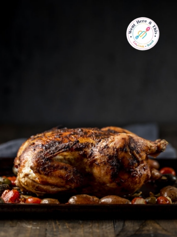 Whole roasted Moroccan chicken with crispy spiced skin, served with roasted tomatoes and olives on a baking sheet.