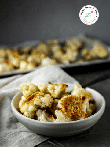 Crispy baked parmesan cauliflower florets with golden, roasted edges in a grey bowl. This easy roasted cauliflower recipe makes a healthy, delicious vegetarian side dish perfect for quick family weeknight dinners.