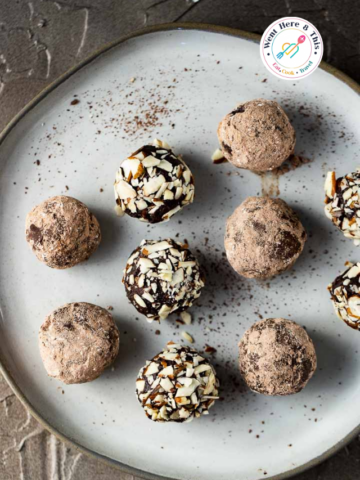 Overhead view of round homemade chocolate truffles on a light grey ceramic plate, with some coated in rich dark cocoa powder and others rolled in chopped almonds.