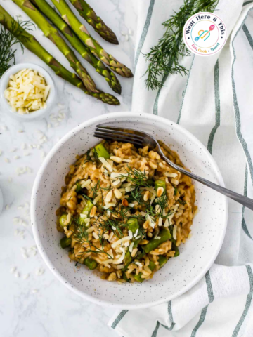 Bowl of creamy lemon asparagus risotto topped with parmesan cheese, pine nuts, and fresh dill, served with fresh asparagus spears.
