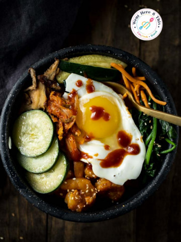 Top-down view of a Korean Bibimbap Bowl featuring a fried egg, gochujang sauce, sliced zucchini, kimchi, and spinach over rice.