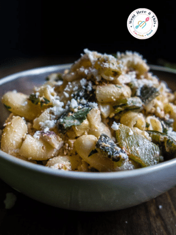 A close-up view of a bowl filled with Mexican Street Corn Pasta Salad, showing elbow macaroni noodles tossed with chunks of roasted green poblano peppers and topped with crumbled cotija cheese.