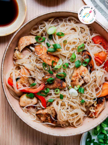 Bowl of Pad Woon Sen (Thai glass noodle stir fry) with chicken, red bell peppers, carrots, and onions, garnished with fresh green onions.
