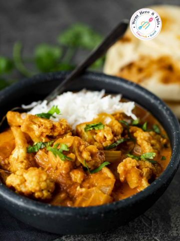 Close-up of Roasted Cauliflower Tikka Masala Curry in a black bowl with white rice, fresh cilantro garnish, and garlic naan.