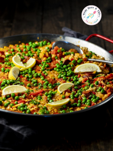 Vibrant traditional Spanish chicken and chorizo paella in a large pan, loaded with rice, bright green peas, and lemon wedges, featured on Went Here 8 This.