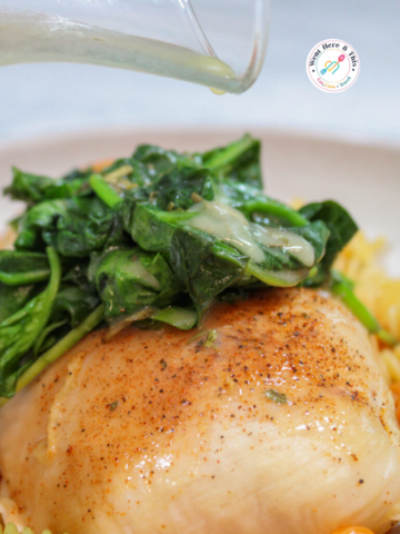 Pouring creamy white wine sauce over pan-seared chicken breast, fresh spinach, and rotini pasta in a white bowl.