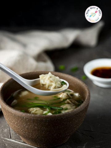 A side-angle close-up of a brown ceramic bowl filled with 20 Minute Wonton Noodle Soup Recipe.
