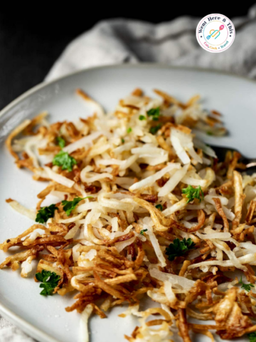 Golden brown, extra crispy shredded air fryer hash browns seasoned with salt and pepper, garnished with chopped fresh parsley, served on a light gray ceramic plate.