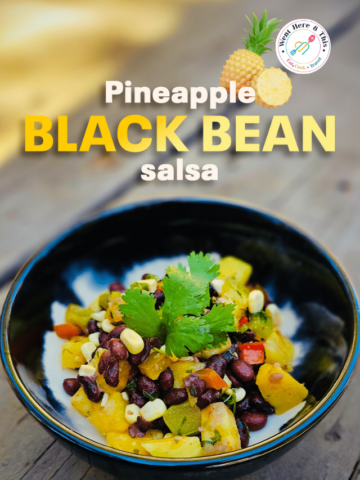 Fresh pineapple black bean salsa in a black ceramic bowl garnished with a fresh cilantro sprig, featuring chunks of sweet pineapple, black beans, corn, and bell peppers.