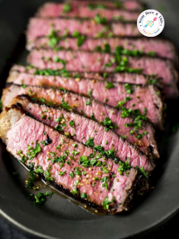 Slices of medium-rare sous vide London broil steak drizzled with a savory Dijon soy glaze and garnished with fresh chopped parsley on a dark platter.