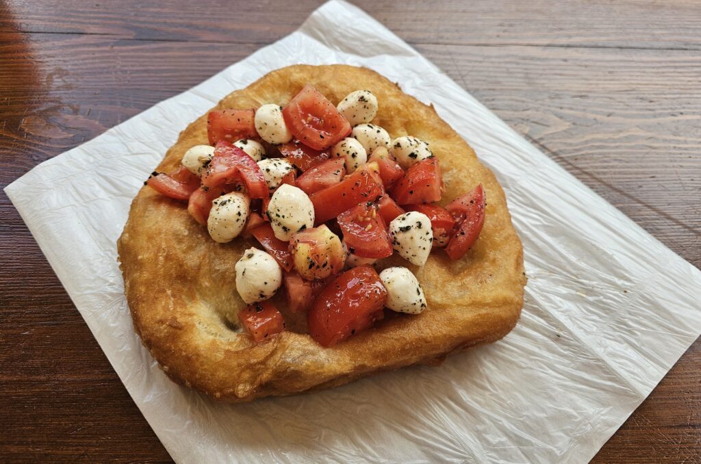 Caprese Lángos is a modern, refreshing fusion twist on traditional Hungarian deep-fried flatbread, topped with fresh tomatoes, mozzarella cheese, and sweet basil.