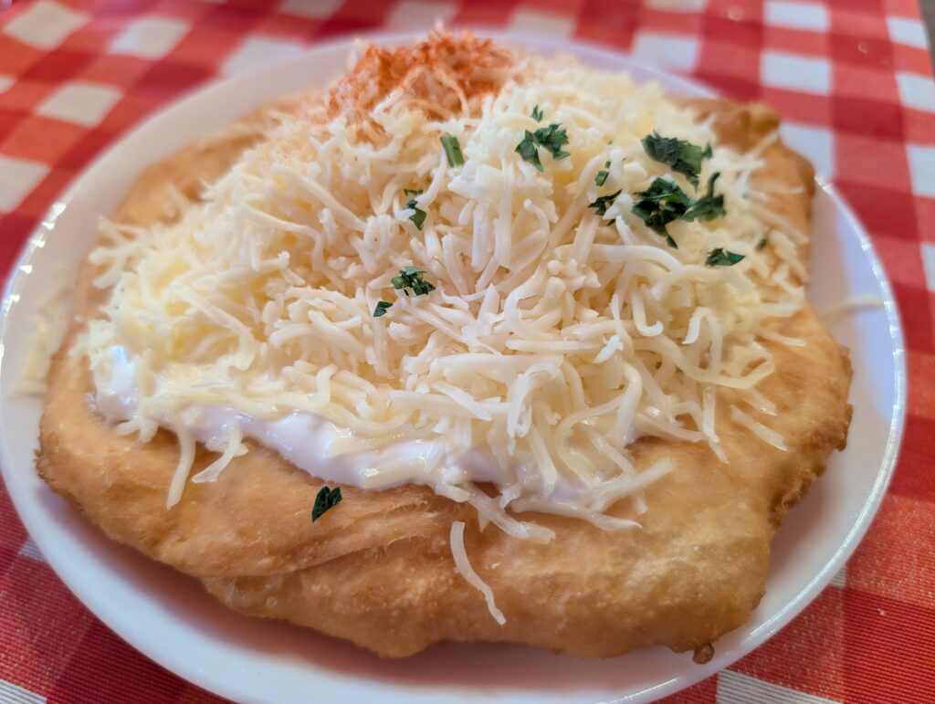 Lángos with sour cream and cheese is a famous Hungarian street food made of deep-fried yeast dough, rubbed with garlic, and topped with cold sour cream and grated cheese.