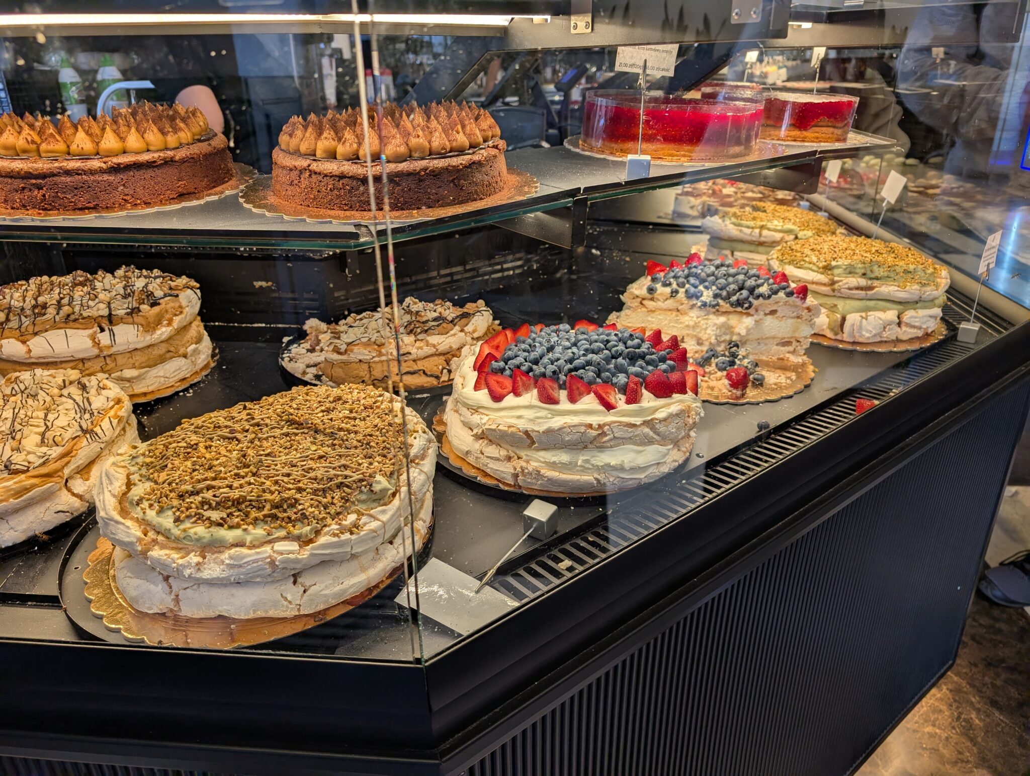 Display case showcasing an assortment of traditional layer cakes, fruit tarts, and towering meringue-based confections.