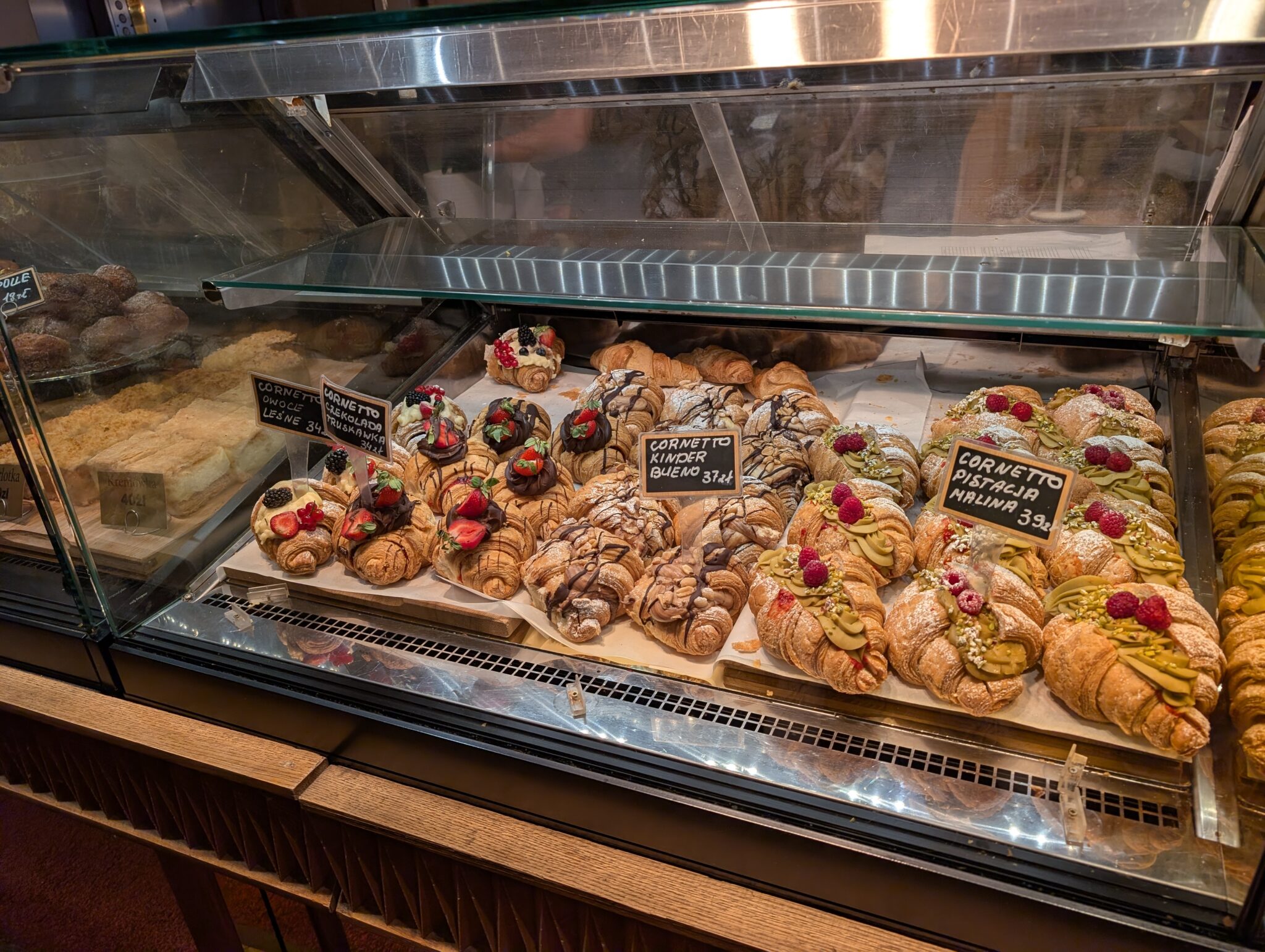 bakery display case features an assortment of filled croissants topped with fruits, chocolates, and creams, including varieties like Kinder Bueno and pistachio-raspberry.