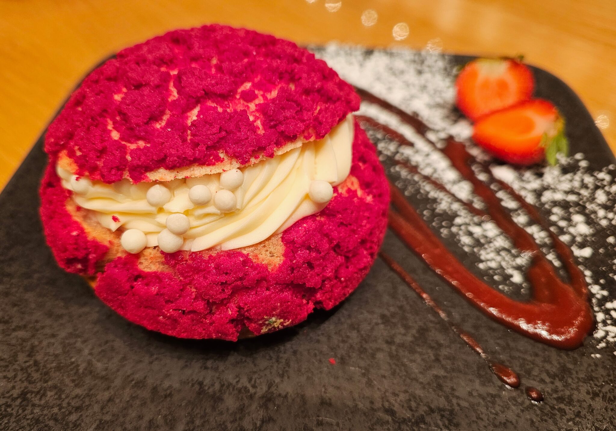 a cream puff featuring a light choux pastry jacket topped with a sweet, crackly crust colored in a vibrant raspberry hue.