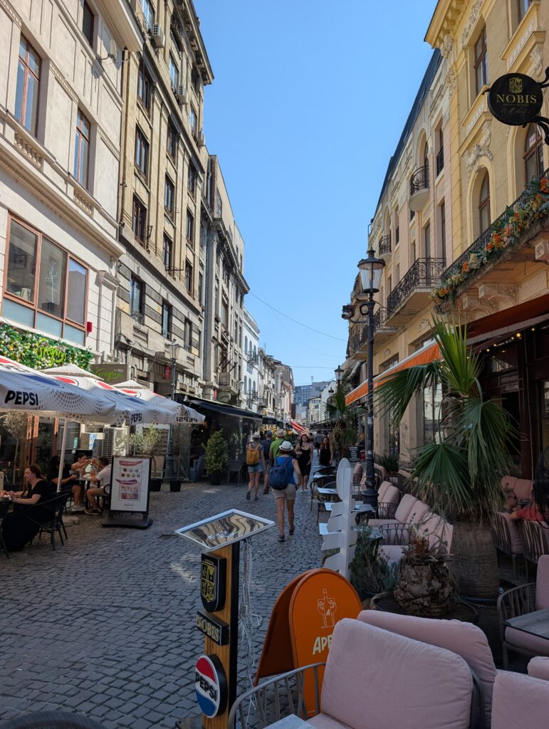 A cobblestone street lined with outdoor cafes and historic multi-story buildings in the Old Town of Bucharest
